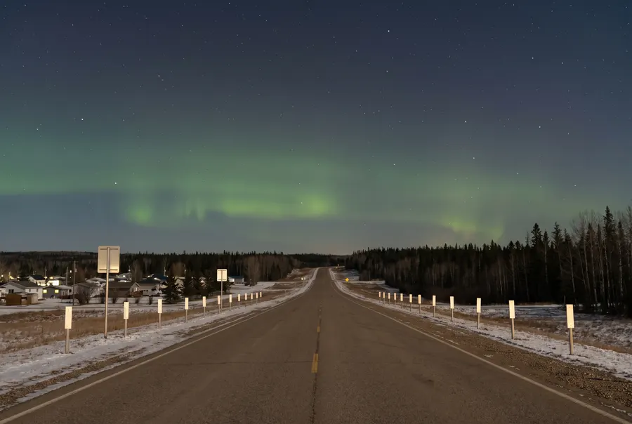 Night highway into the forest under northern lights